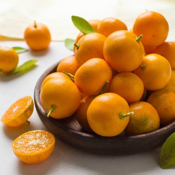 a pile of calamondin oranges on a wooden dish.