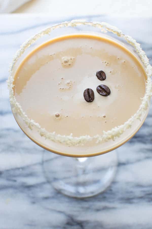 coffee buzz martini in a martini glass with coffee beans floating on the surface.