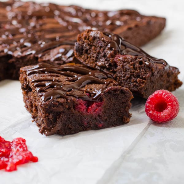 Two slices of Ultimate Raspberry Truffle Brownies that show the interior of the brownie with pops of red raspberry poking out.