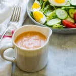a small pitcher of dressing next to a salad.