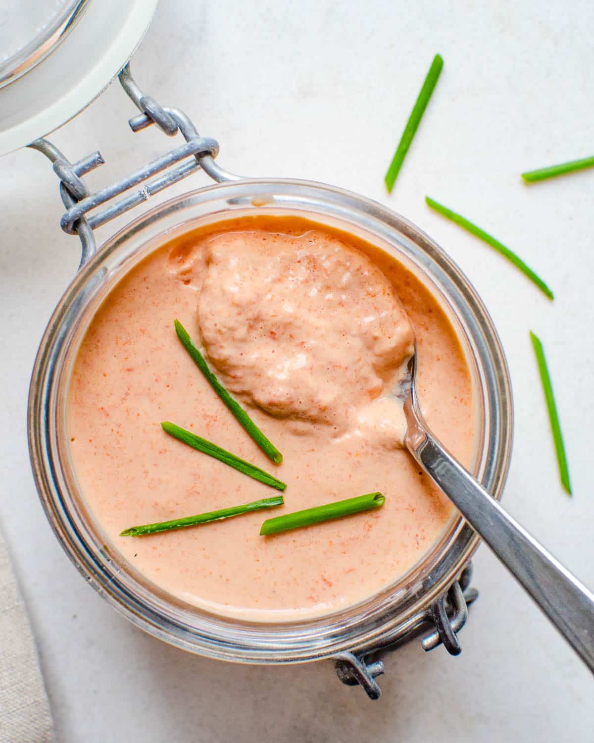 Serving a jar of red pepper aioli with chives on top.