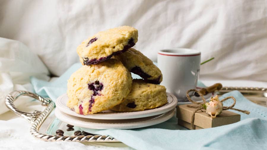 blueberry cream cheese scones on a silver tray with a gift box and cup of coffee.