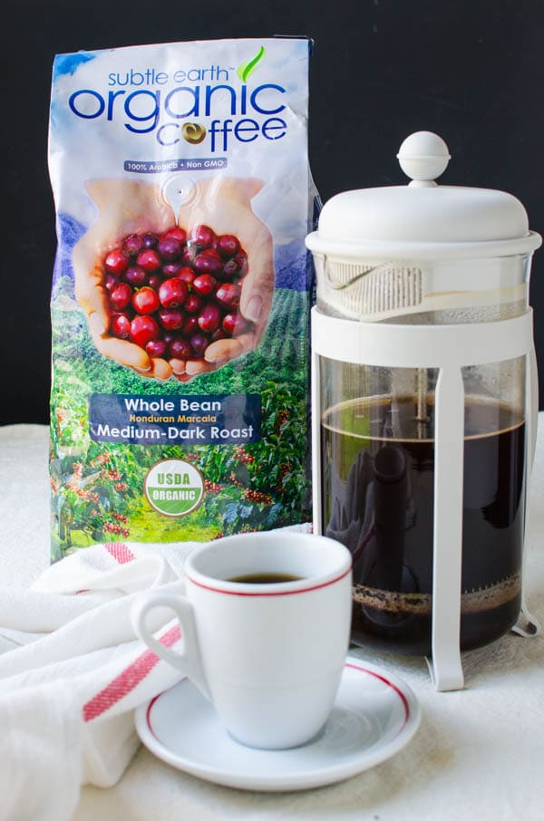 A bag of subtle earth organic coffee with a french press and cup and saucer.