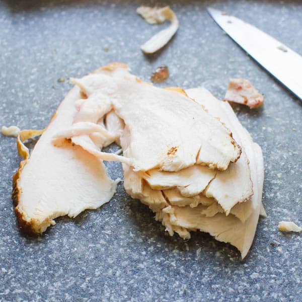 sliced smoked chicken on a cutting board with a knife.