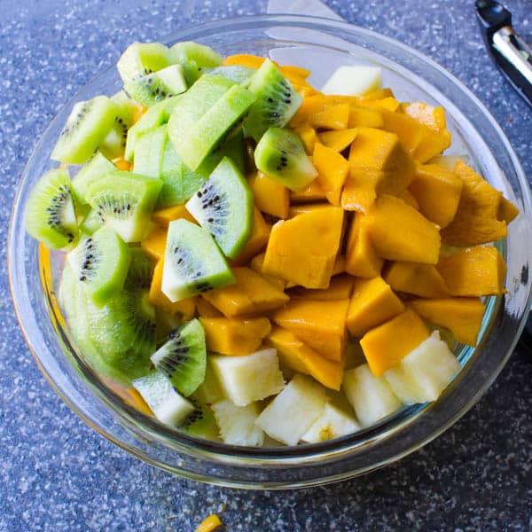kiwi and mango added to the pineapple in a bowl.
