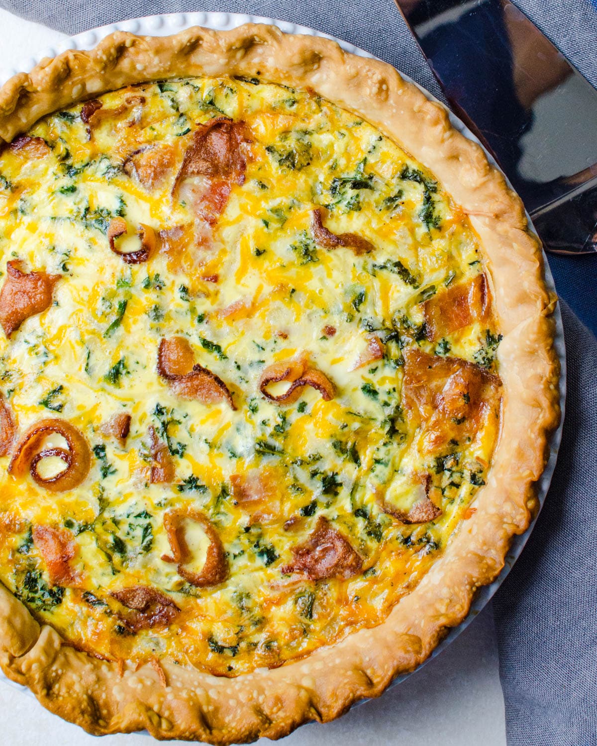 Bacon and kale quiche with a pie server.