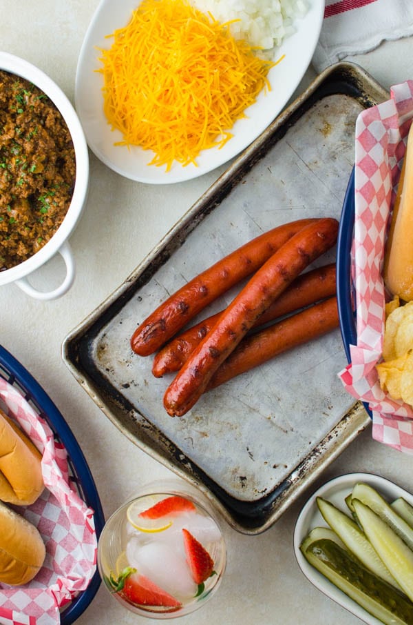 hot dogs, cheese, onions, chili, buns, pickles and drinks.
