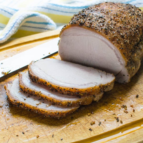 Herb Crusted Pork Loin being sliced on a cutting board.