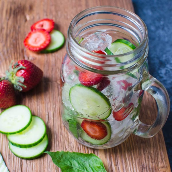 filling the glass with sliced cucumbers and strawberries for basil water, a healthy summer drink.