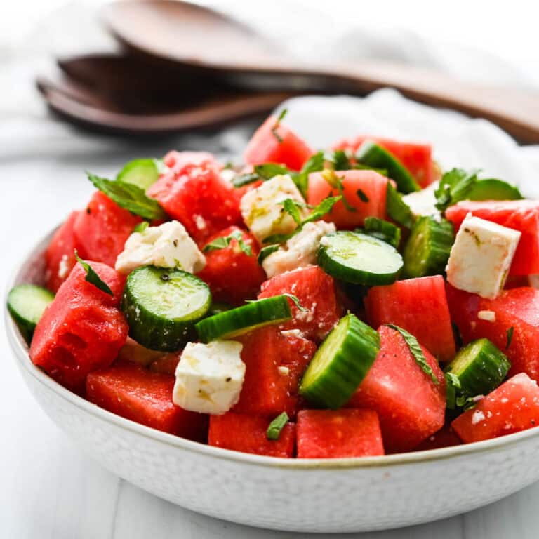Watermelon cucumber salad in a white bowl with fresh herbs.
