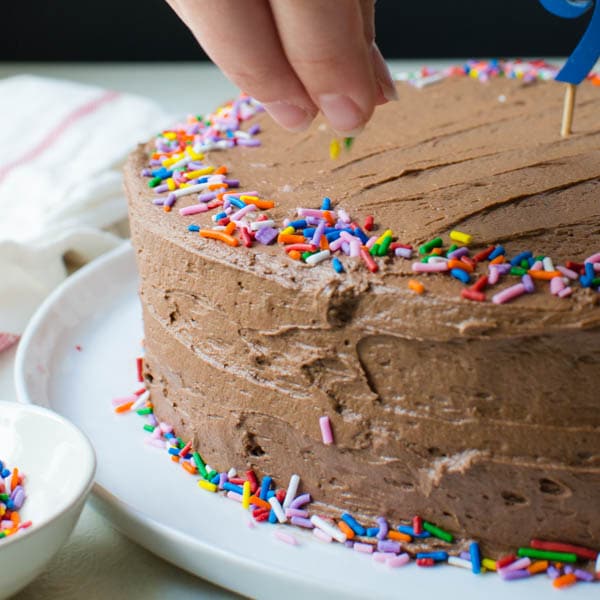sprinkling rainbow jimmies on the easy yellow cake recipe with milk chocolate frosting.