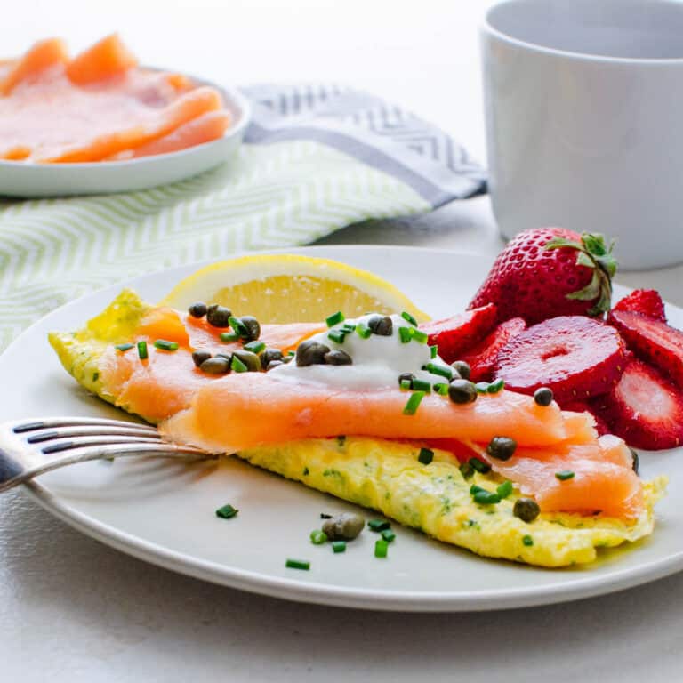 A smoked salmon omelette with creme fraiche on a plate with fresh fruit.