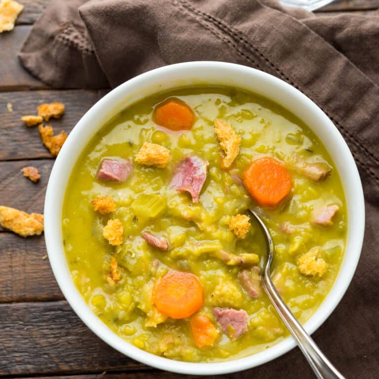 A bowl of pea soup with chunks of ham.