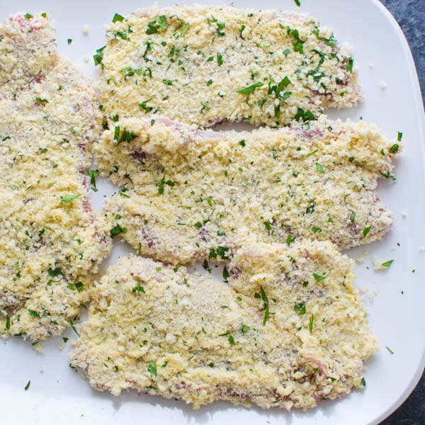 Breaded pork cutlets on a plate before frying. One of the best schnitzel recipes.