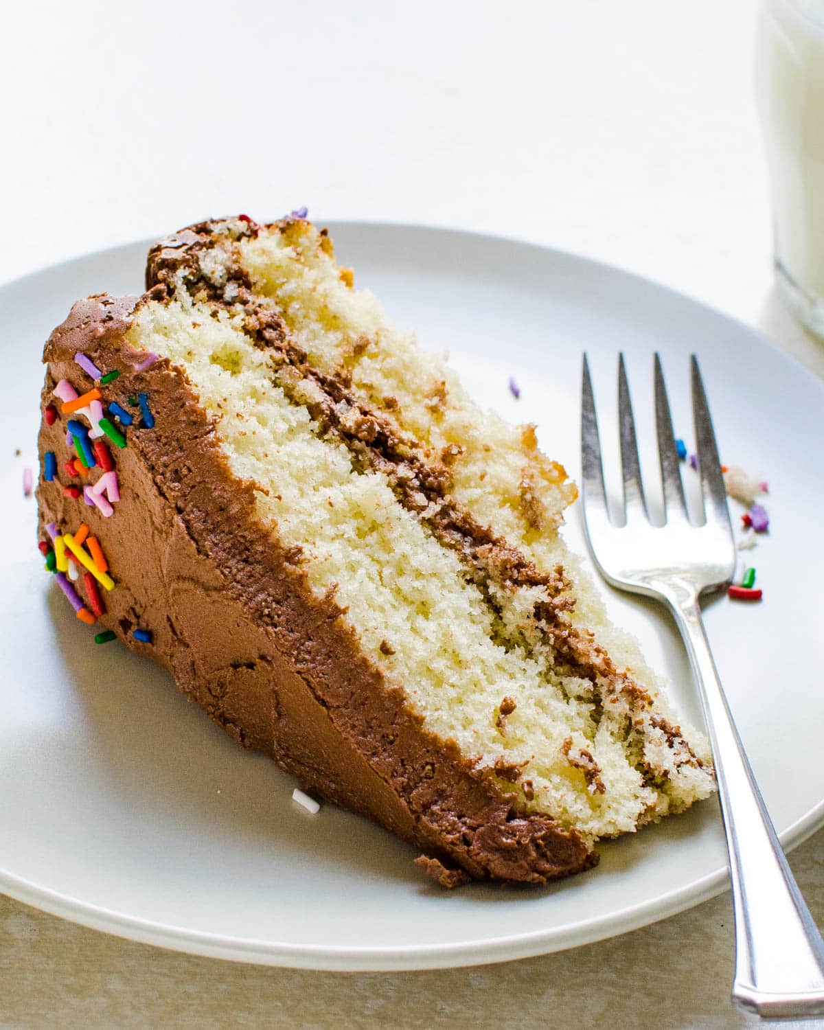 A slice of yellow cake with chocolate frosting and sprinkles.