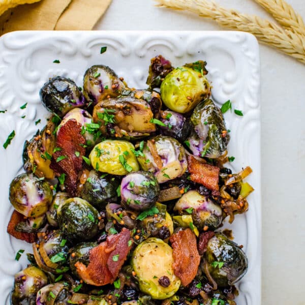 Tangy Glazed Brussels Sprouts on a serving platter with bacon crumbled over the top.