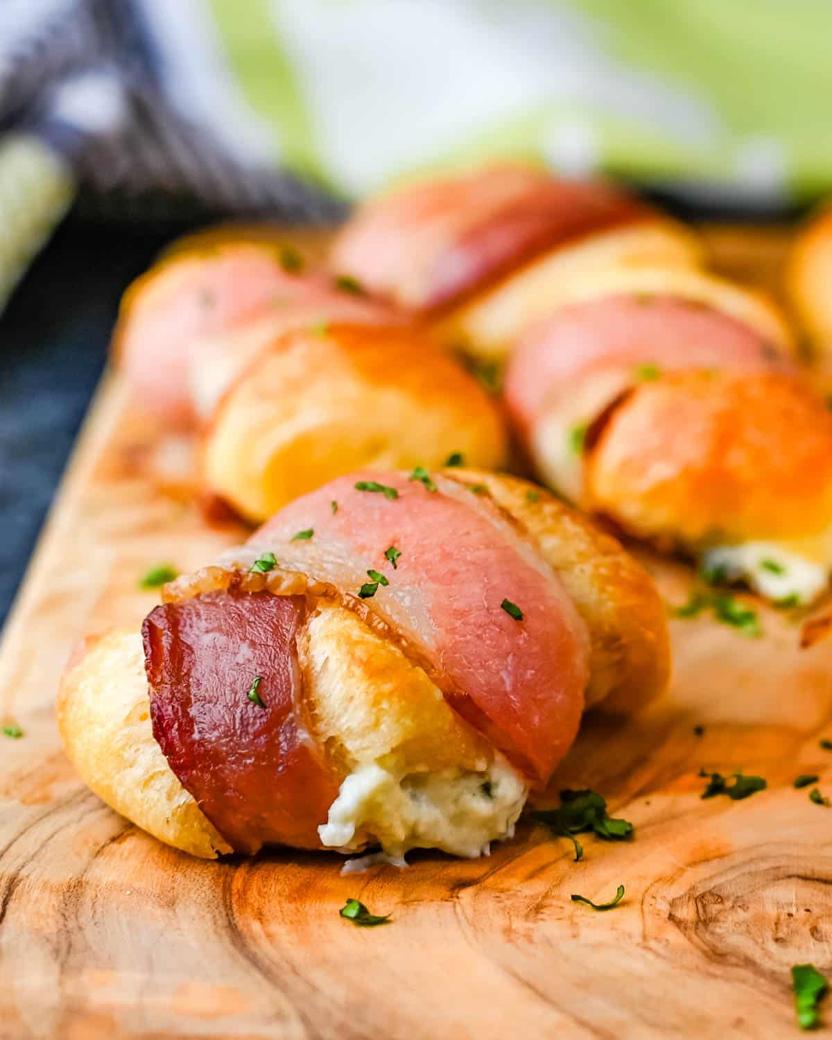 Bacon-wrapped cream cheese crescent rolls on a wooden board.