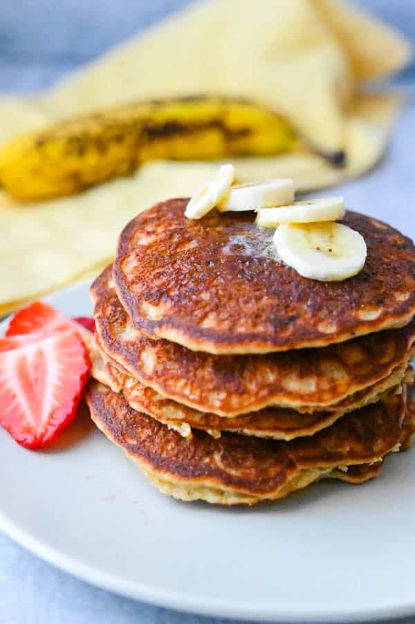 a stack of pancakes topped with butter, sliced bananas and strawberries.