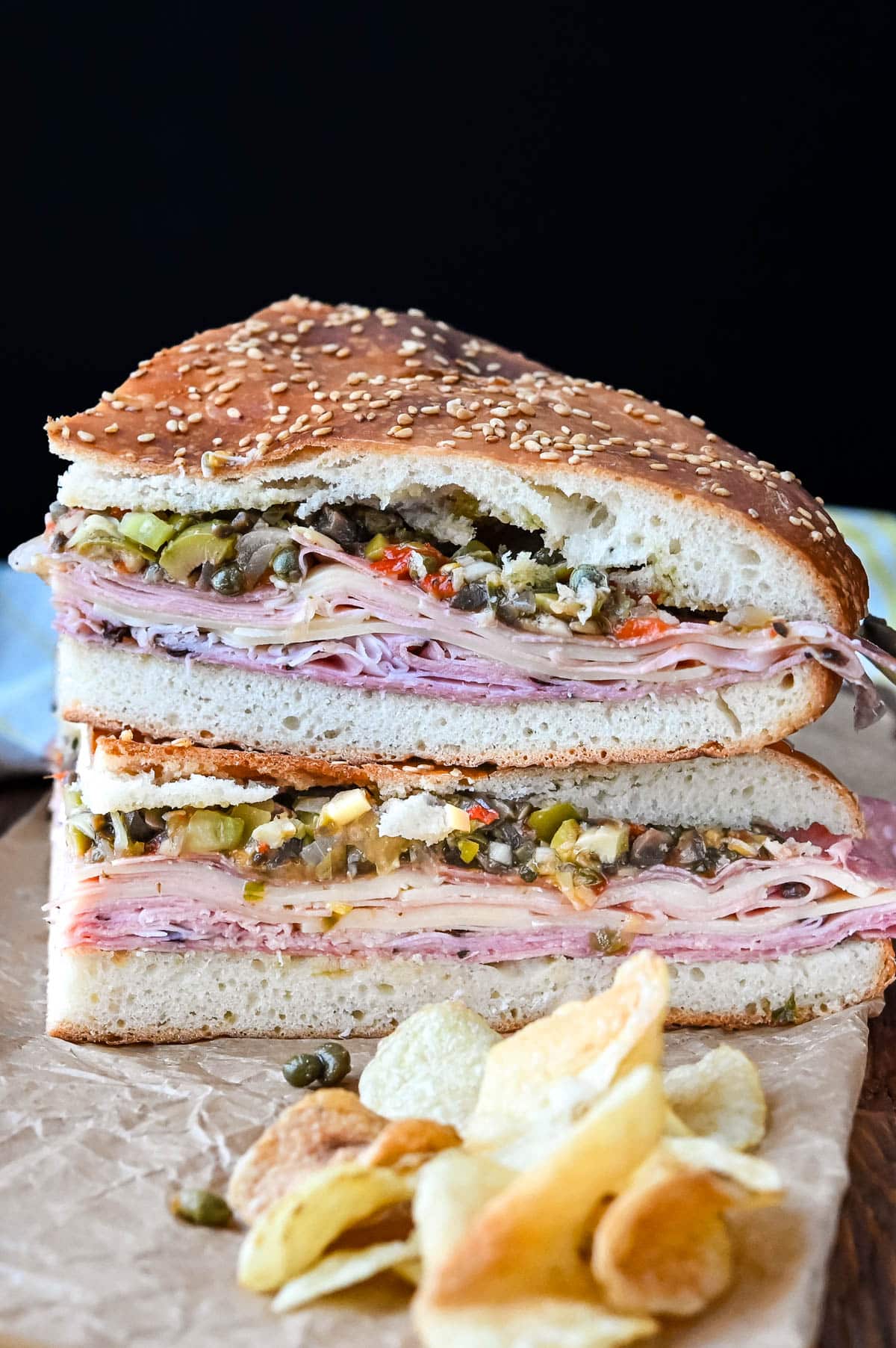 Sliced muffuletta sandwiches stacked on each other with a side of chips.