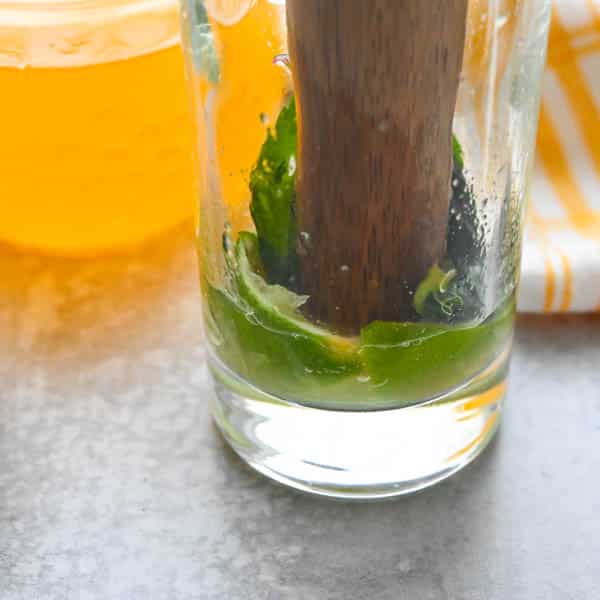 muddling lime and mint in a highball glass.