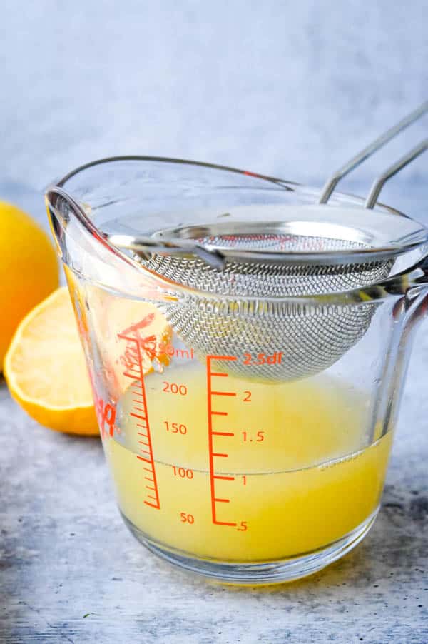 Squeezing lemon juice from lemons and straining to remove pulp and seeds for sparkling lemonade.