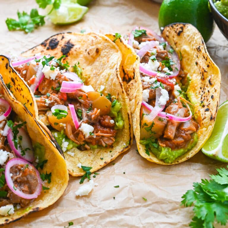 Three tinga tacos dressed with queso fresca, pickled onions and cilantro.