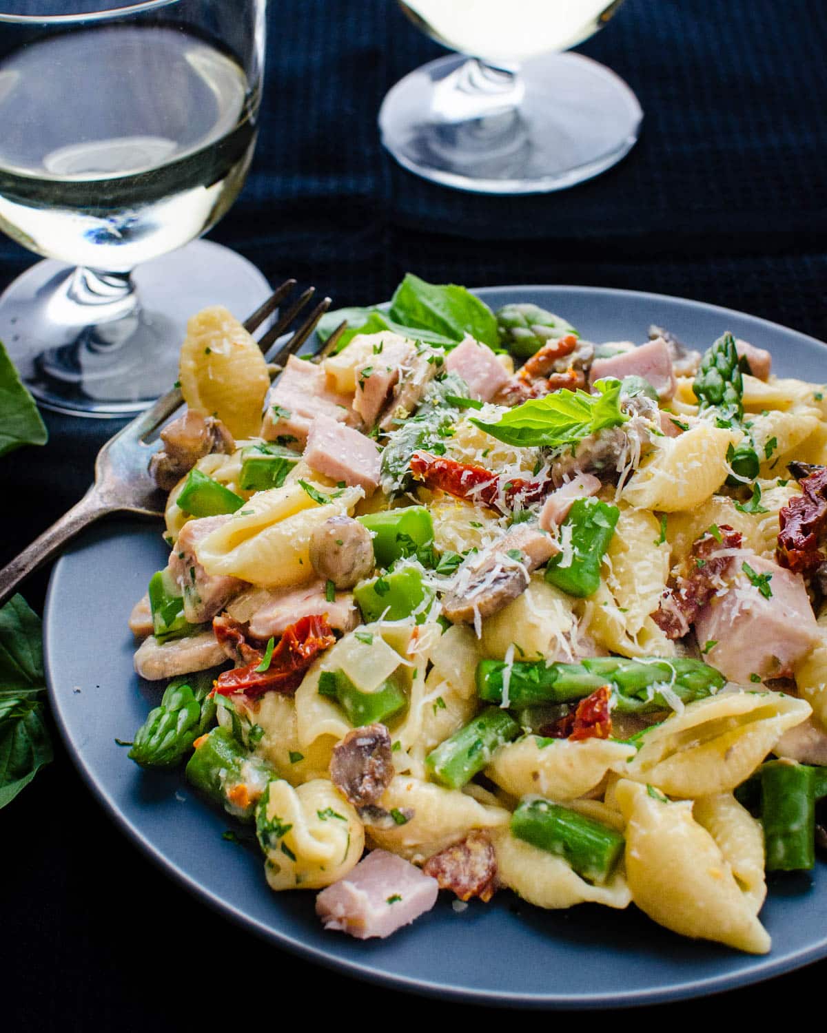 A plate of pasta primavera with asparagus, ham and sun-dried tomatoes.