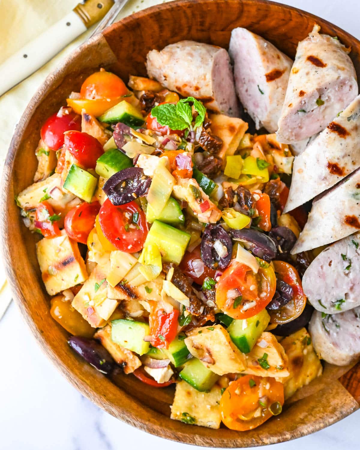 Serving grilled chicken sausage and panzanella salad in a wooden serving bowl.