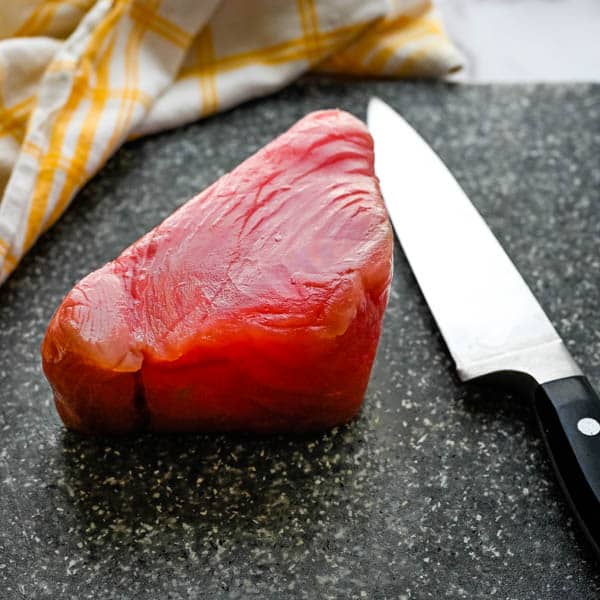 a piece of fresh ahi tuna on a cutting board with a knife.