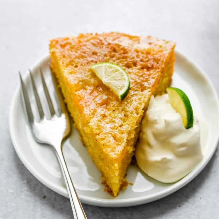 mango cake on a white plate with whipped cream and lime slice.