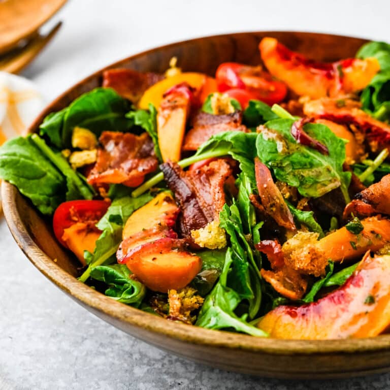 serving peach and baby kale salad with bacon in a wooden bowl.