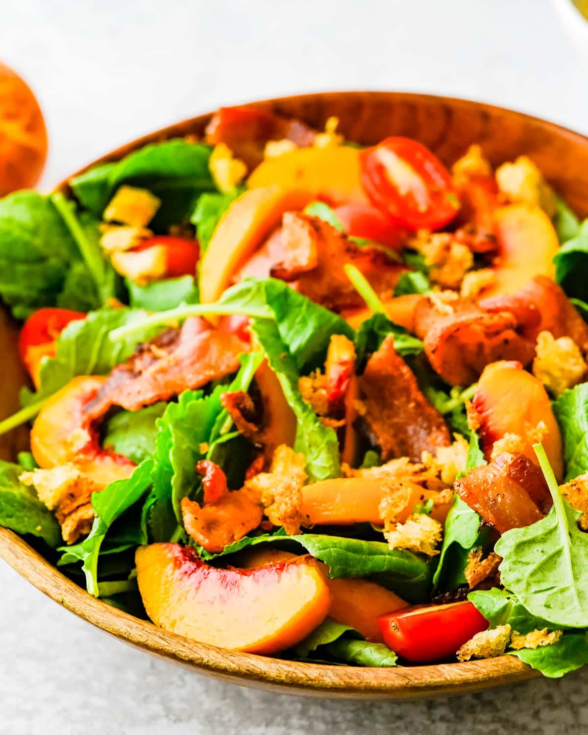 A bowl of peach and kale salad with bacon.