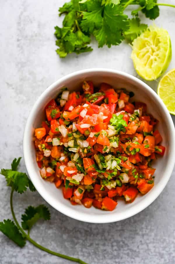 Serving Best pico de gallo recipe in a white bowl with a squeeze of lime. This is an easy fresh tomato salsa recipe.