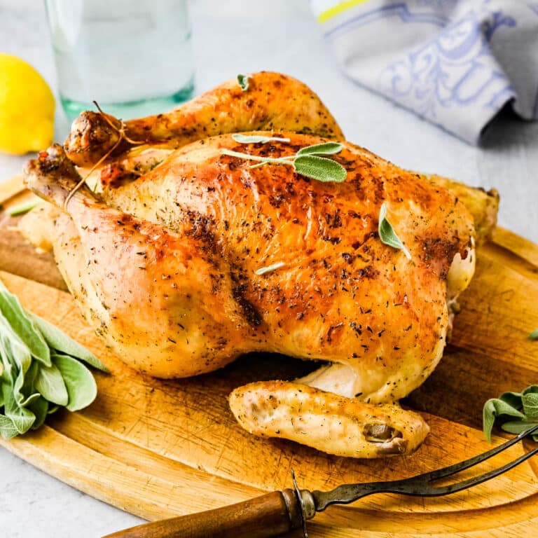 roasted chicken on a cutting board with fresh herbs.