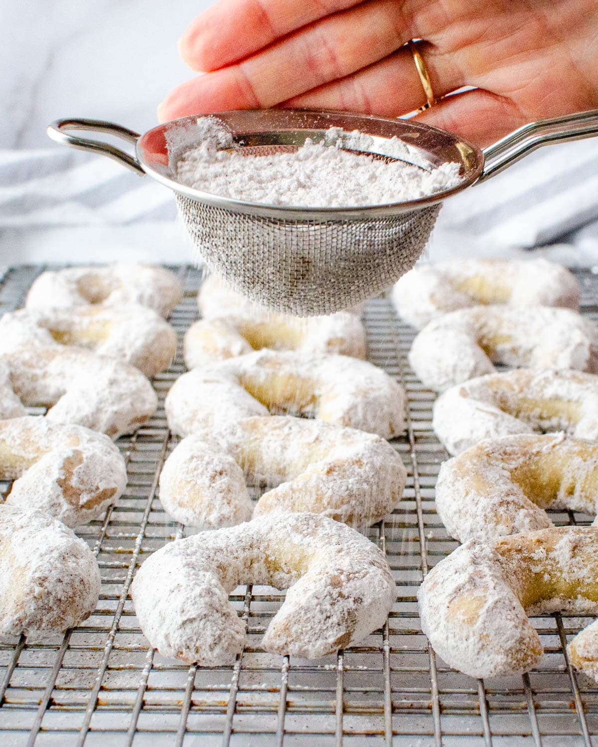 Sprinkling the tops of the almond crescent cookies with powdered sugar mixture. 