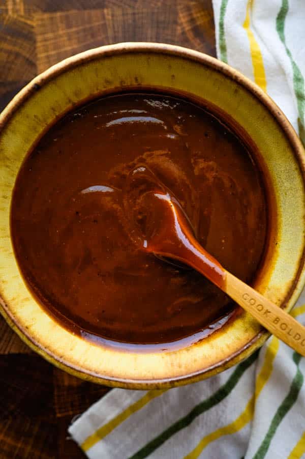 Homemade BBQ sauce for ribs in a bowl with a wooden spoon.