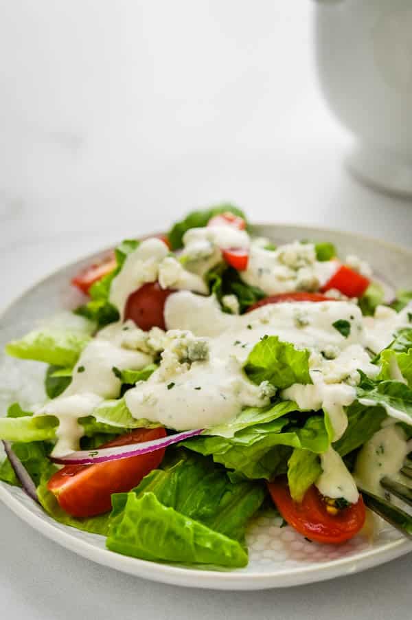 pouring homemade blue cheese dressing on a salad.