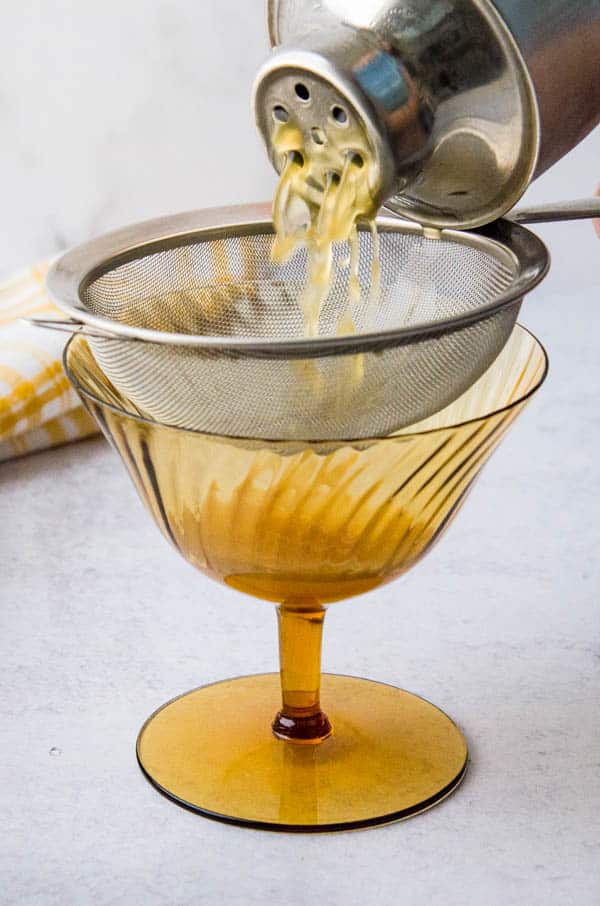 straining ginger bourbon blend through a fine mesh strainer.