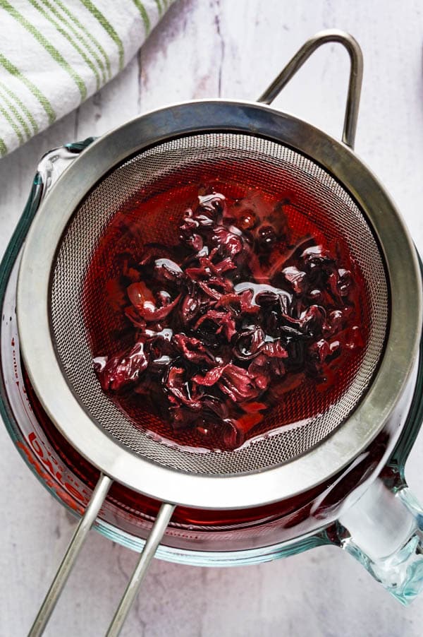 straining the dried hibiscus flowers from the liquid.