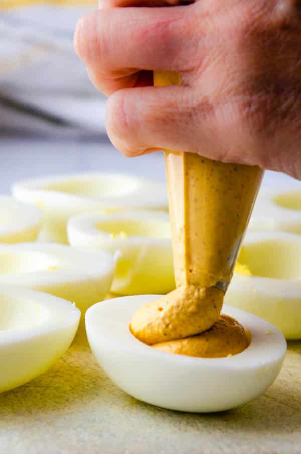piping spicy egg yolk filling into the deviled eggs.
