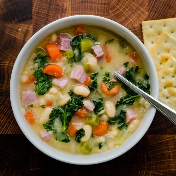 ham, kale and northern bean soup in a bowl with saltine crackers.