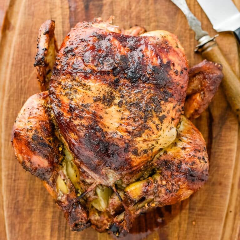 A grilled rotisserie chicken resting on a wooden cutting board.