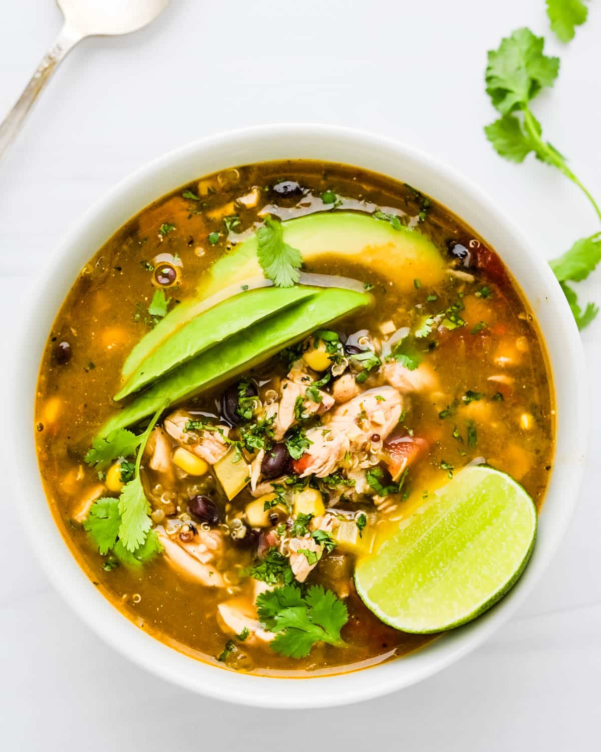 A bowl of chicken taco soup with avocado, lime and fresh cilantro.