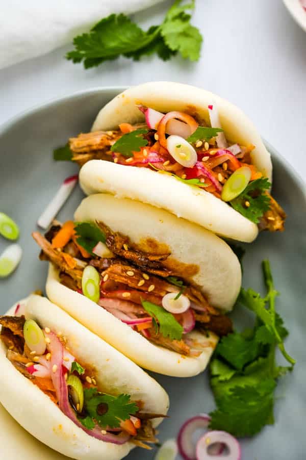 Fully dressed pulled pork buns with cilantro, scallions, sesame seeds and pickled onions.