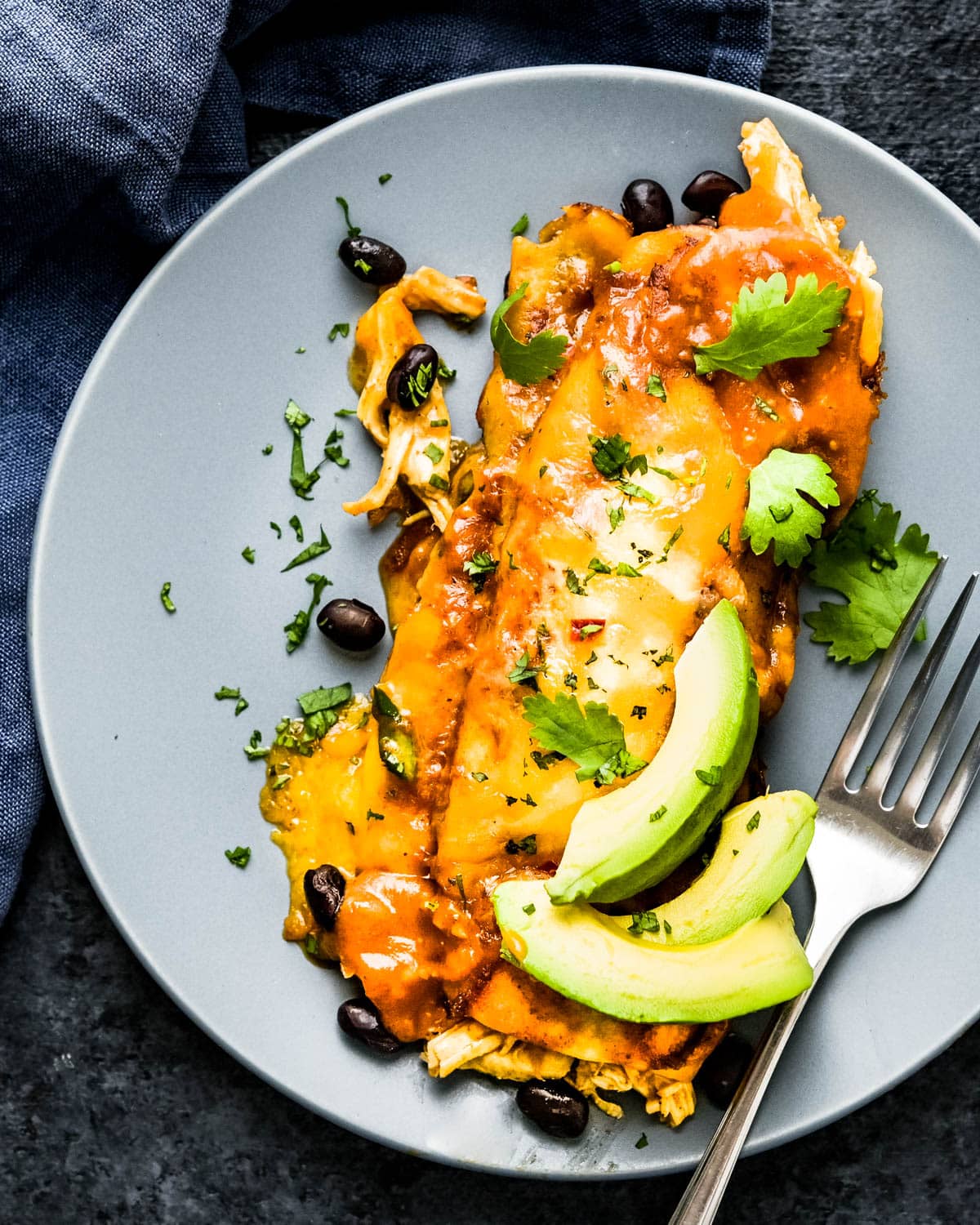 A chicken and black bean enchilada with slices of avocado and plenty of cheese.