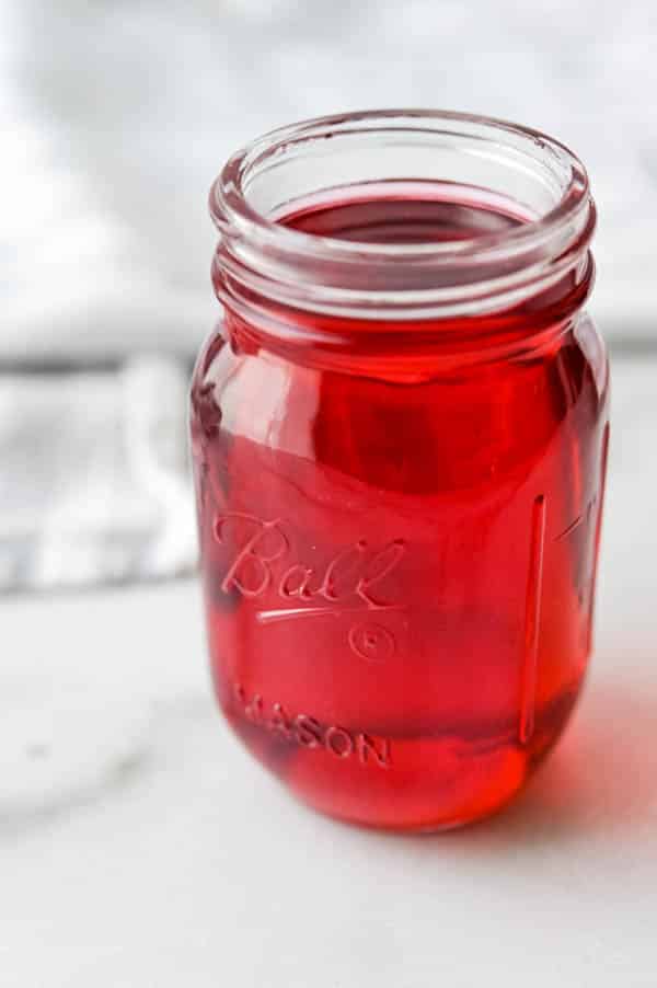 A jar of hibiscus simple syrup is candy-apple red.