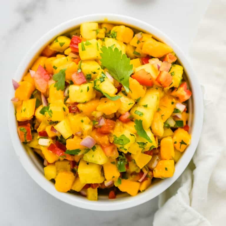 A bowl of pineapple mango salsa with a white napkin beside it.