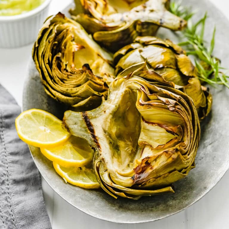 Grilled artichokes with slices of lemon on the side.