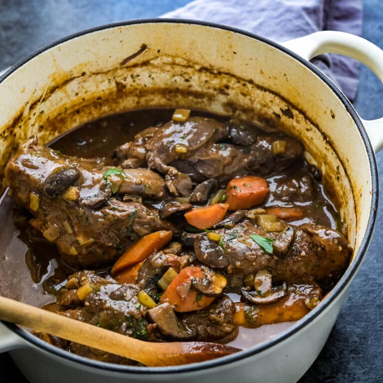A dutch oven filled with braised lamb shanks and carrots in a sauce.