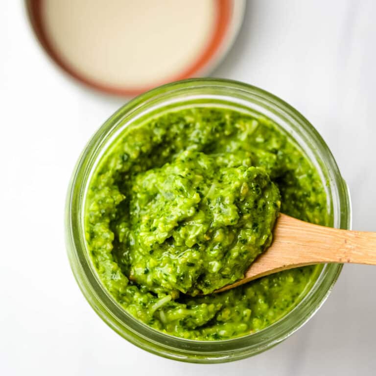 a wooden spoon scooping spinach pesto from a jar.